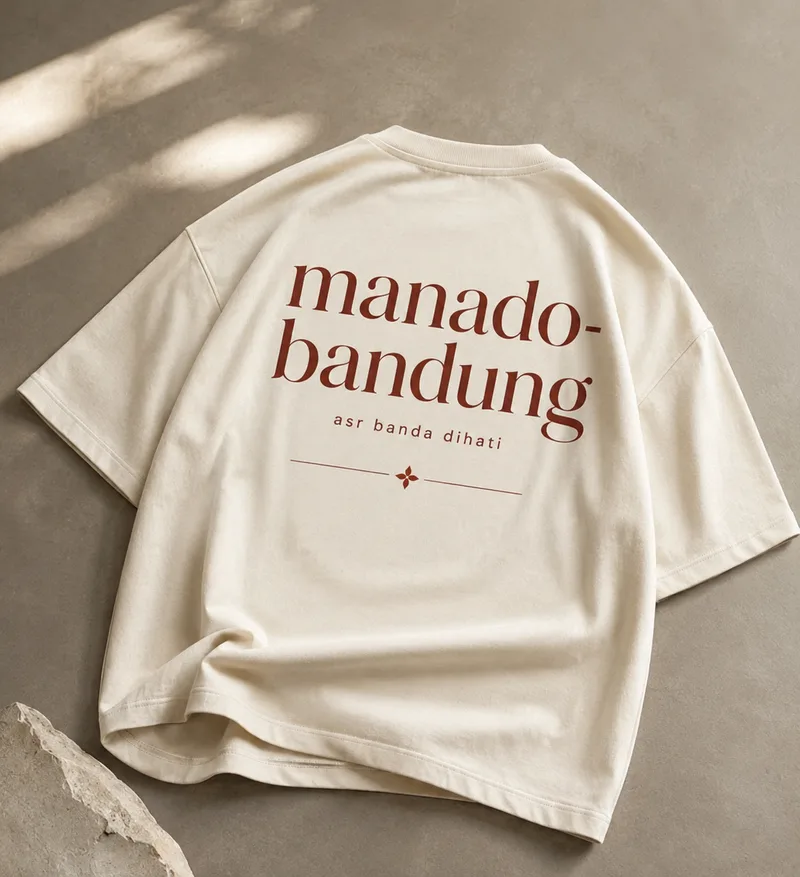Kaos oversize warna krem dengan sablon punggung "manado-bandung" dan tulisan "asr banda dihati" — dua kota yang dijembatani asrama ini.